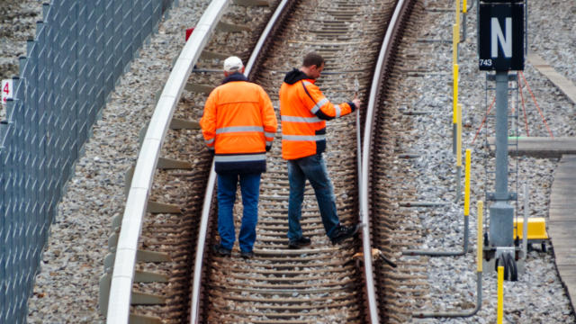 两名身穿橙色高能见度夹克的工人在铁路上工作